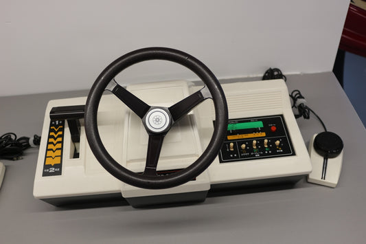 A steering wheel on a table next to a remote control